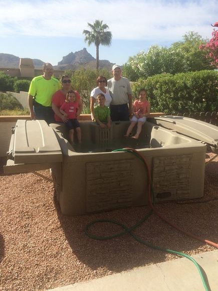 Family gathered around their newly placed spa with mountains behind
