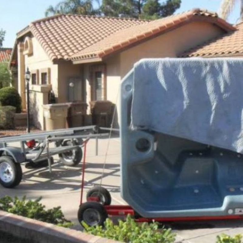 Hot tub strapped to a red moving dolly in a driveway